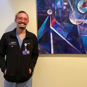 A male Northwestern Medicine ICU physician standing next to a piece of art he created on a wall.