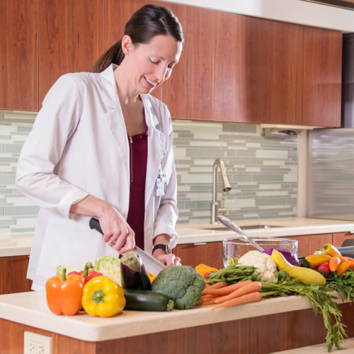 Woman in a lab coat chopping vegetables.