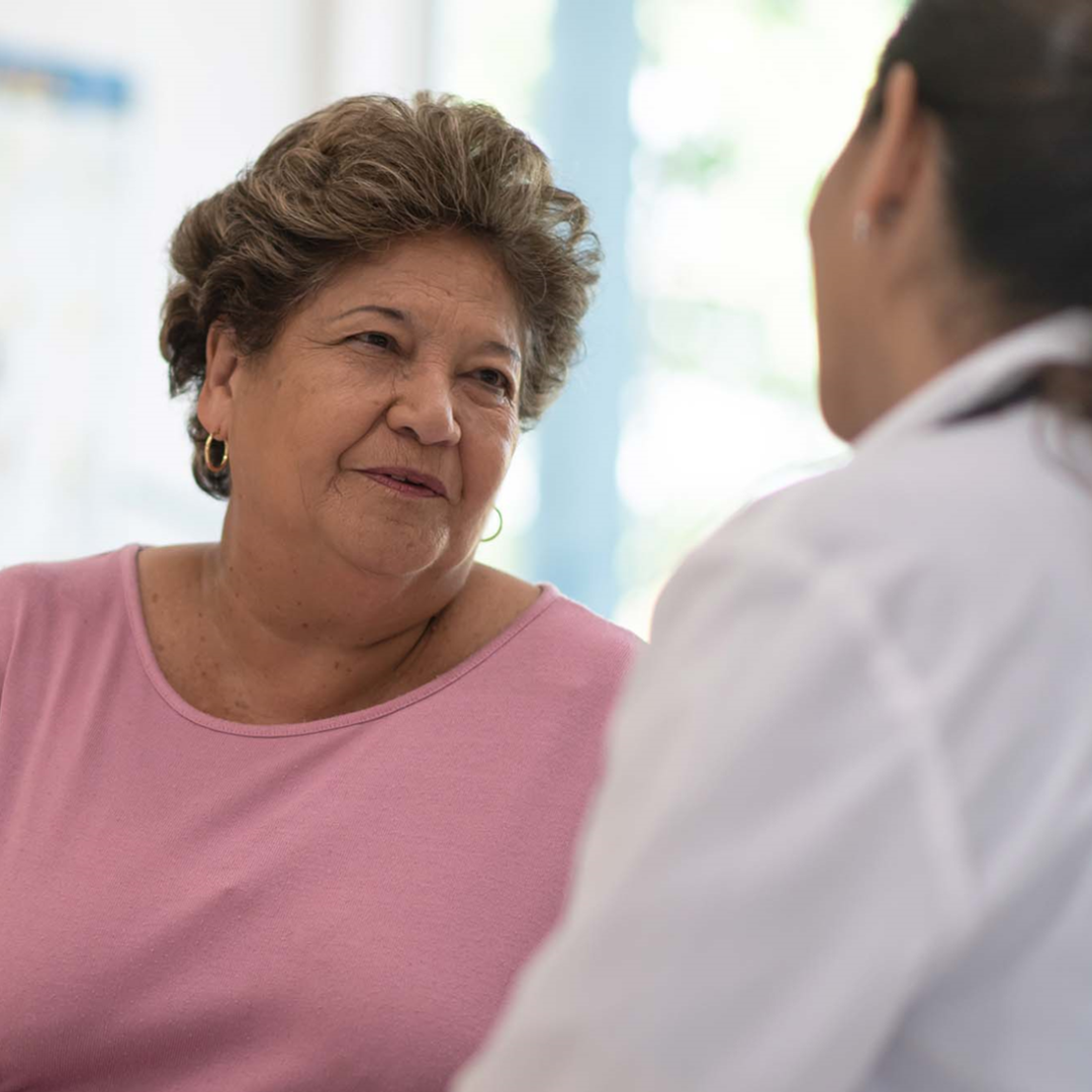 Female patient in a pink shirt talking with a female healthcare provider who is wearing a white coat.