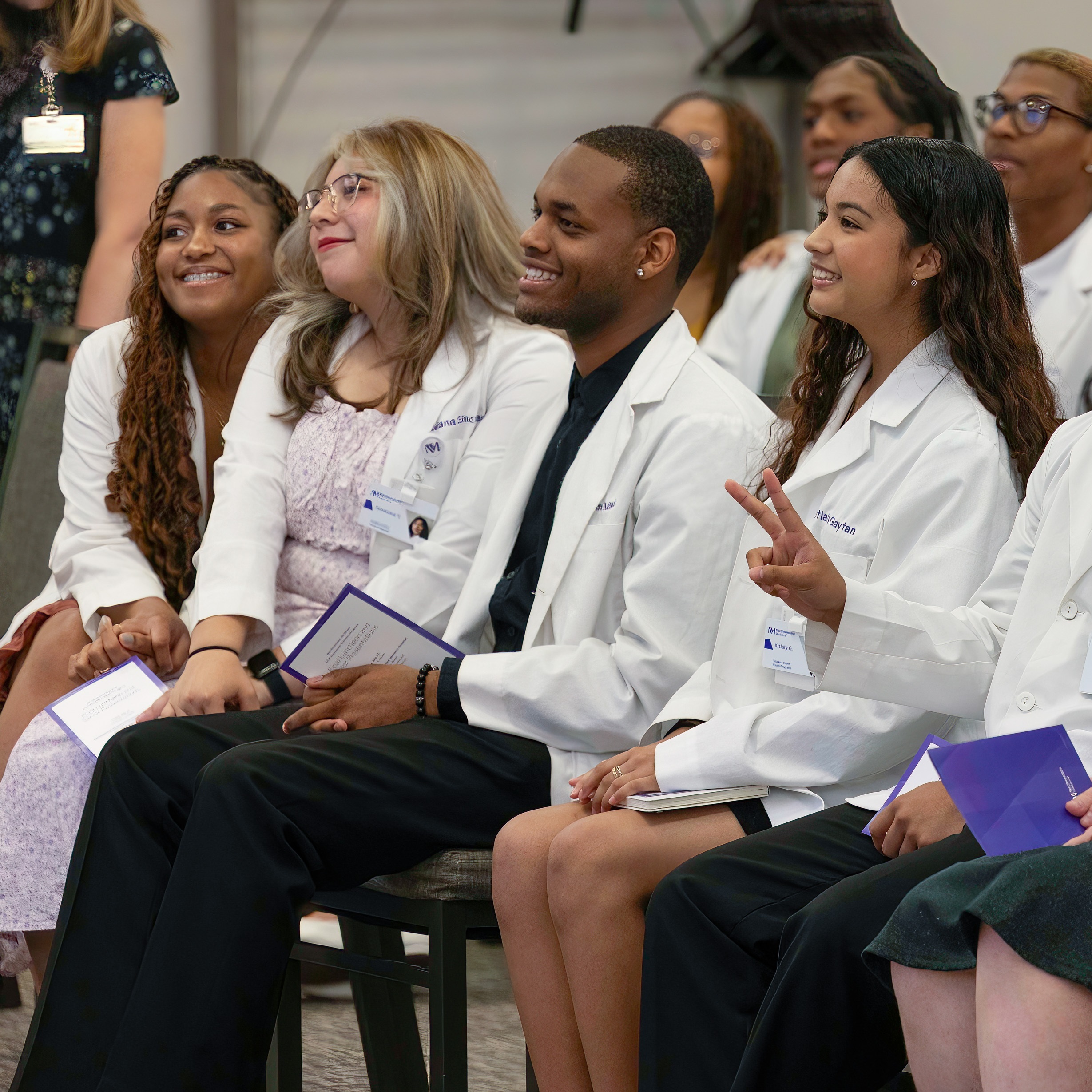 Students in the Scholars program sitting in an assembly wearing their white coats