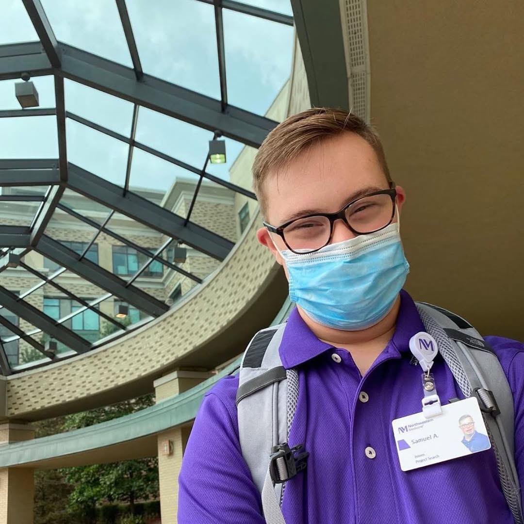 Photo of a man wearing a mask and glasses standing underneath a glass rotunda.