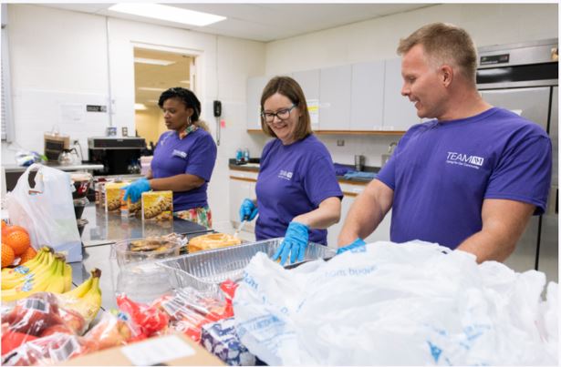 Team NM Volunteers in purple shirts helping put food into bags.