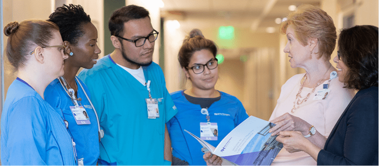 NM Workforce participants wearing scrubs talking with an NM clinician in a hallway.