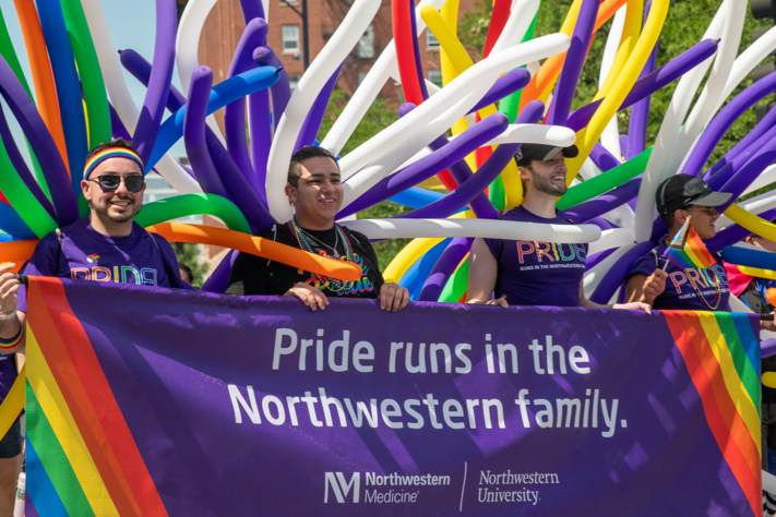 NM employees carrying a purple banner that says "Pride runs in the Northwestern Family."
