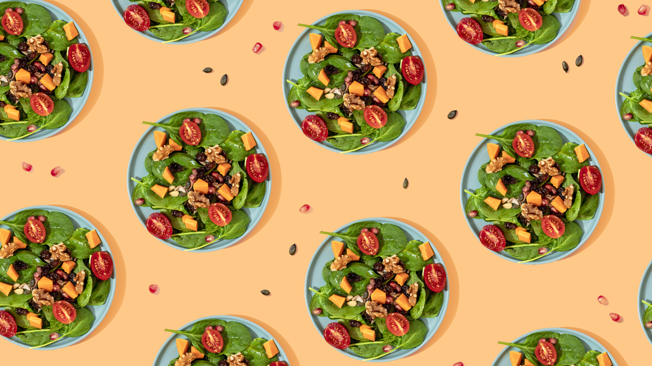 Multiple small blue circular dishes with spinach leaves topped with tomatoes and walnuts.