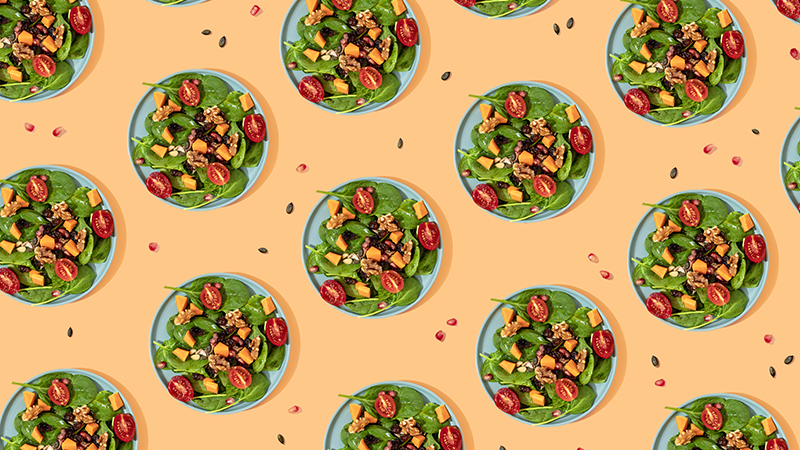 Multiple small blue circular dishes with spinach leaves topped with tomatoes and walnuts.