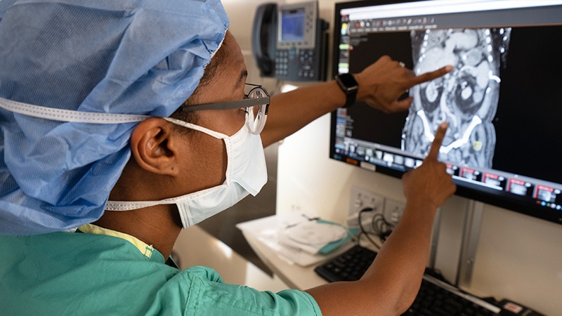Dinee C. Simpson, MD, wearing surgical scrubs and pointing to an X-ray image on a computer screen.