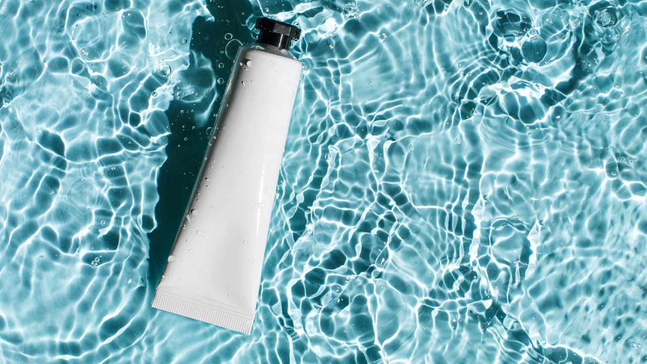 Tube of sunscreen floating in a light blue pool with rippled water.