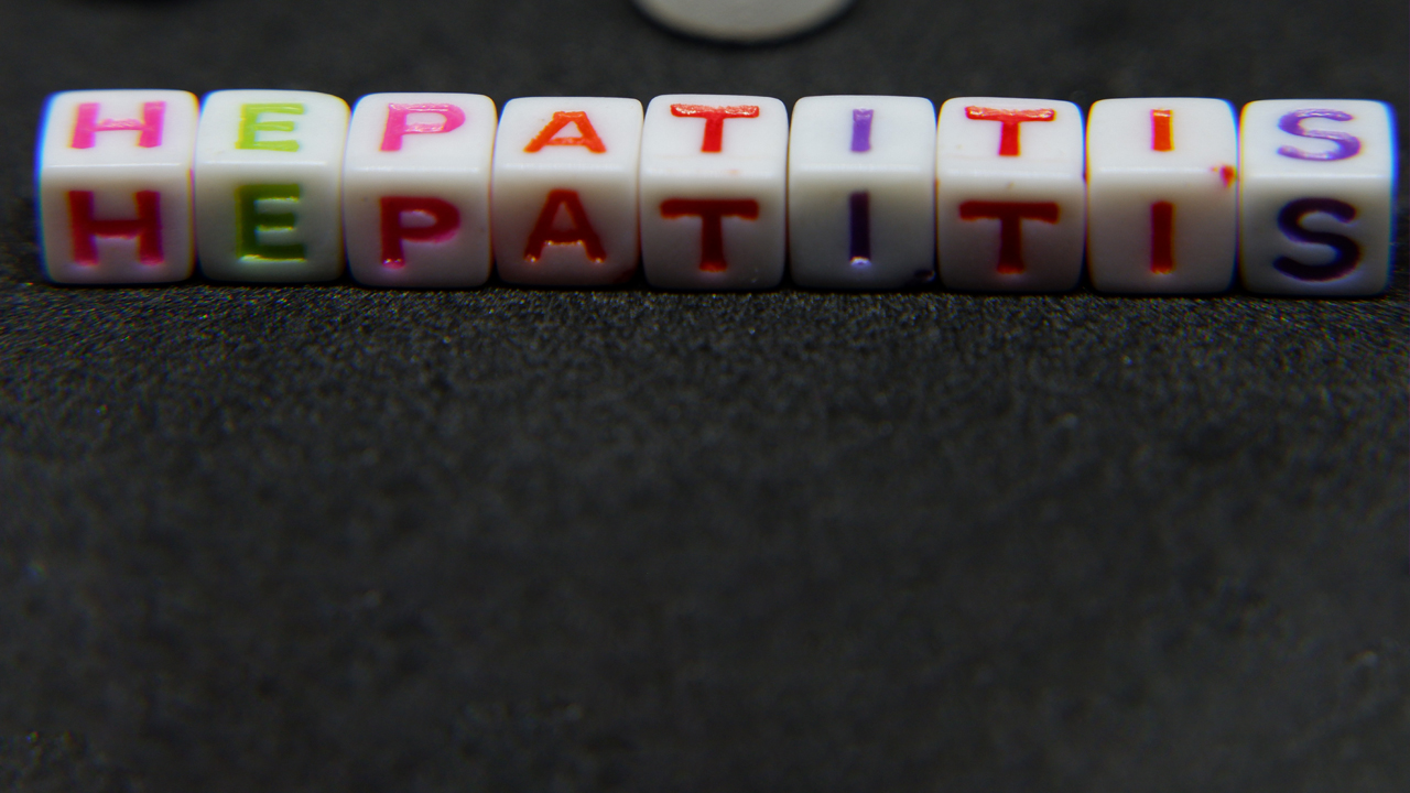 Photo of white plastic block letters on a dark background spelling Hepatitis in pink, green, red and purple.