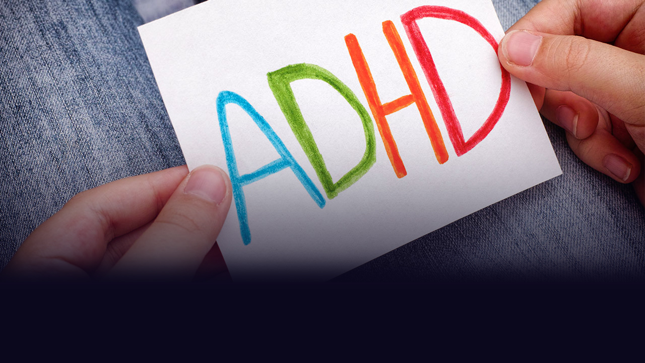 Person holding a small piece of paper with "ADHD" written, each letter in a different color.
