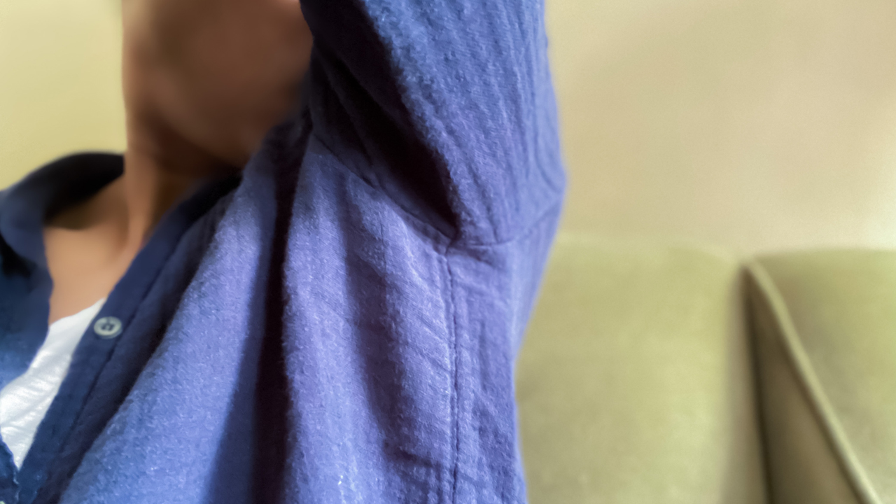 A person wearing a blue buttoned shirt smelling their armpit. 