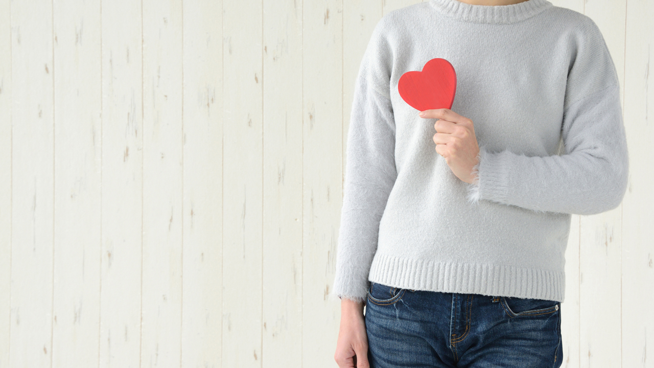Person, pictured from the neck down, wearing a great sweater and holding a red item shaped like a heart.