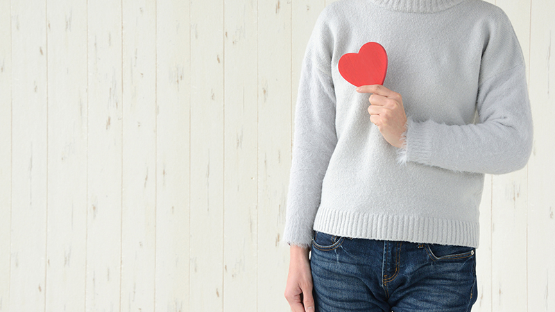 Person, pictured from the neck down, wearing a great sweater and holding a red item shaped like a heart.