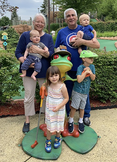Two grandparents enjoying time with their four grandchildren at a miniature golf course.