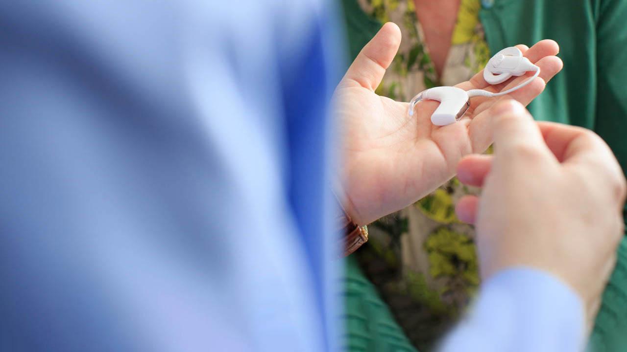 Person in scrubs holding a cochlear implant with a patient.