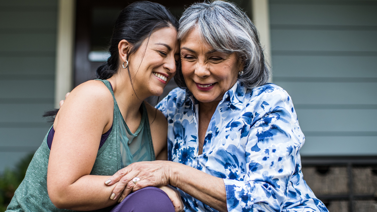 Two people embracing each other and smiling with a house in the background.