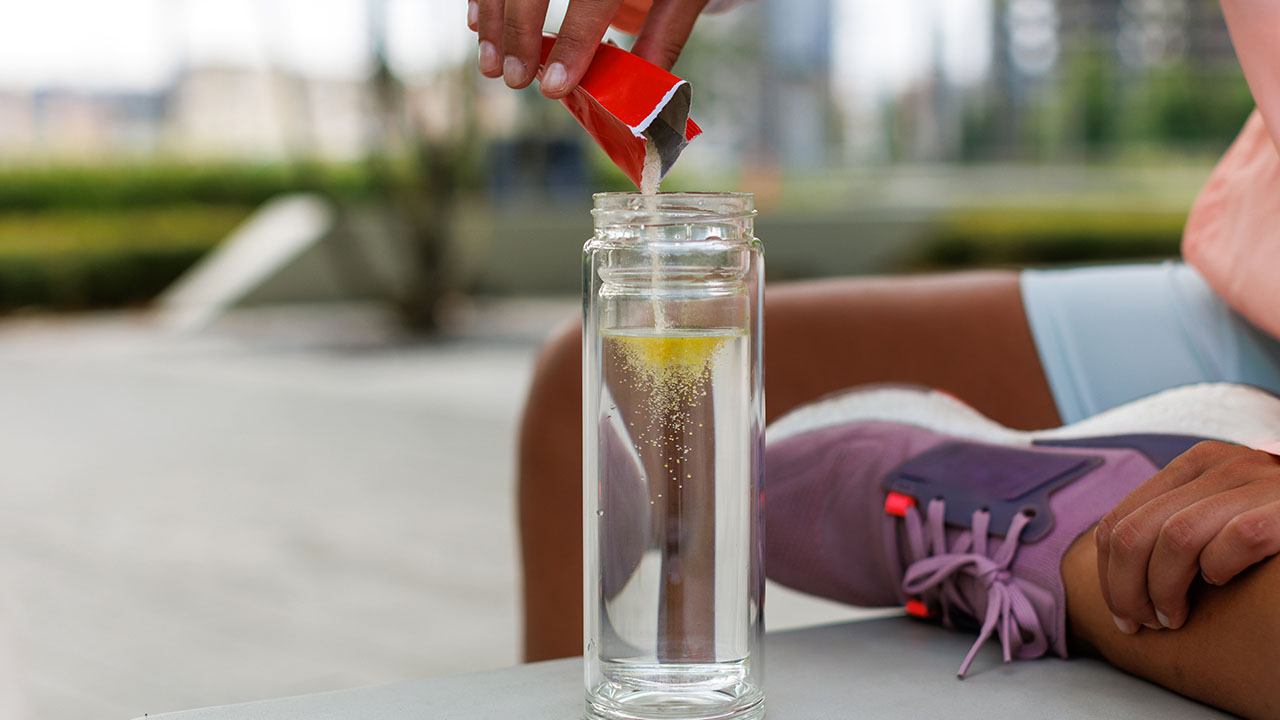 Young athlete pouring electrolyte powder into a water bottle.