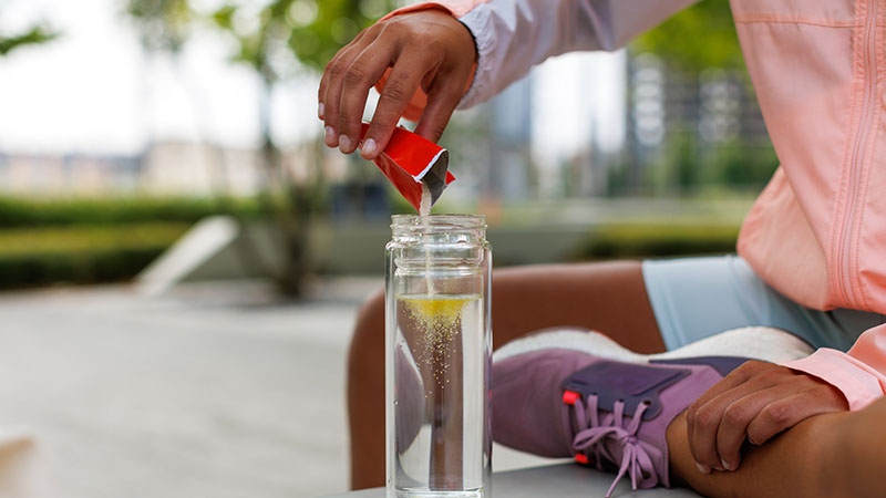 Young athlete pouring electrolyte powder into a water bottle.