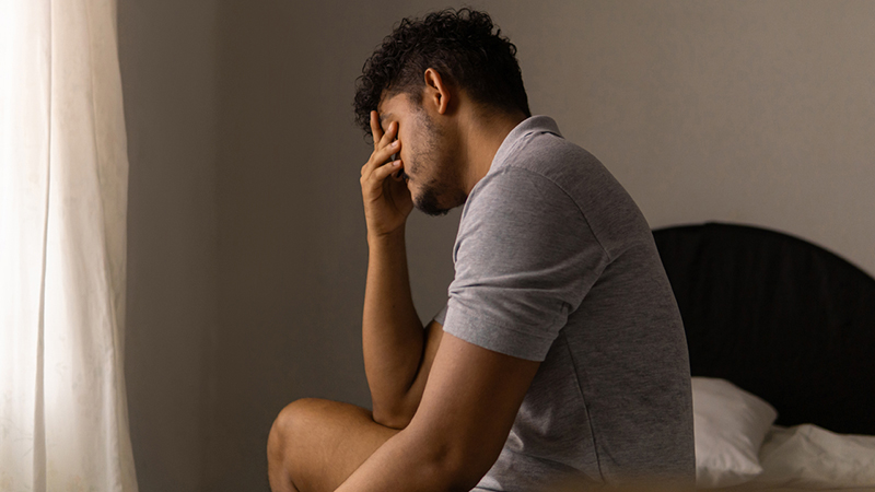 Person holding their face while sitting in bed, as if with a headache.