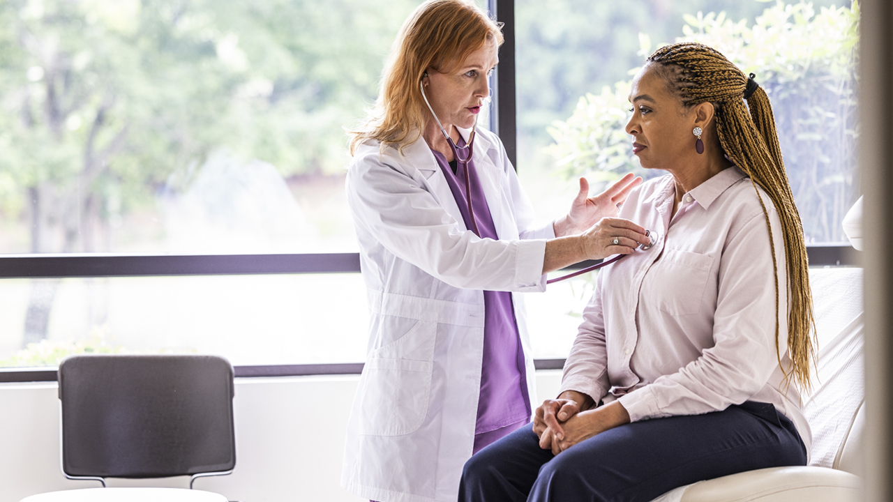A doctor listening to a patient’s heart in an exam room.