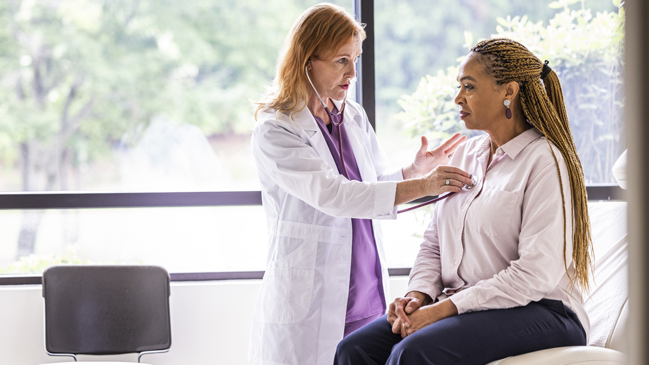 A doctor listening to a patient’s heart in an exam room.