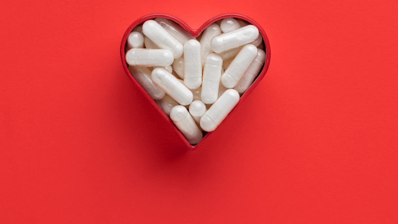 Heart-shaped container filled with white supplements on a red background.