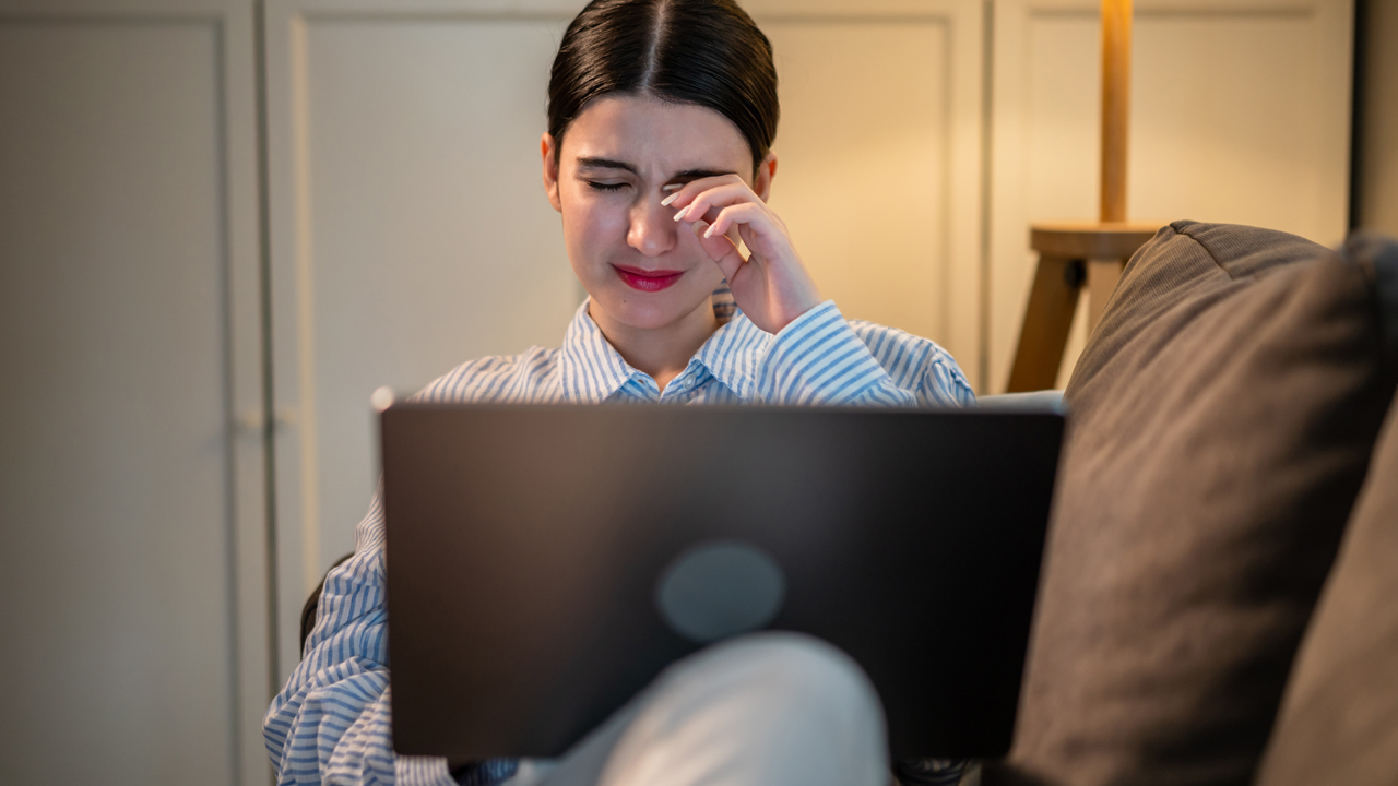 A person sitting at their laptop rubbing their eye. 