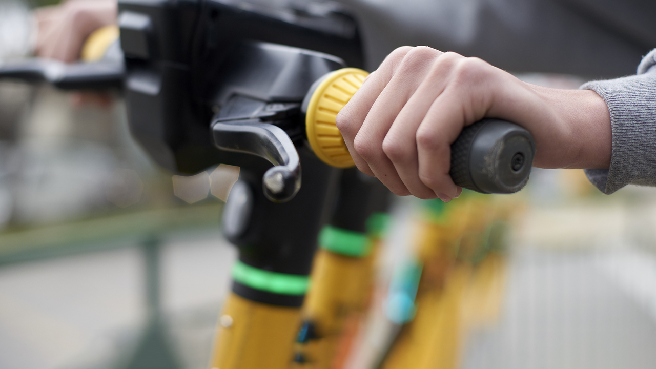 Person gripping handlebars of an electric scooter.
