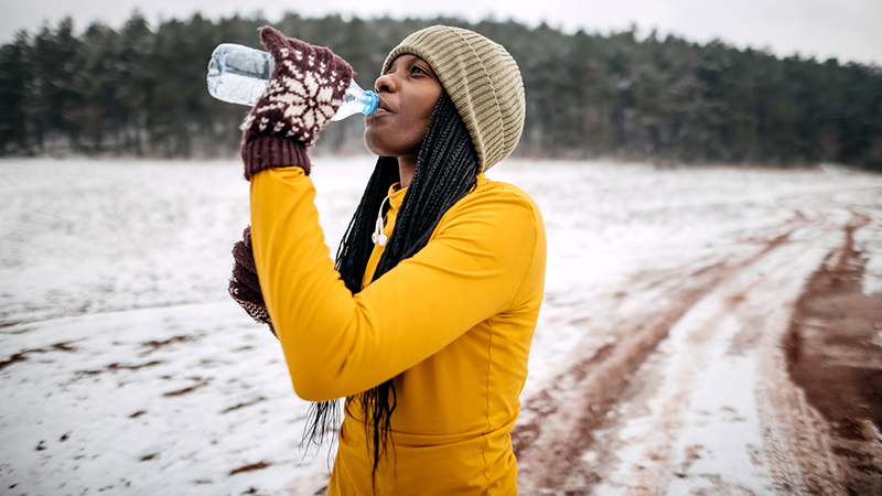Woman in winter work out clothes drinking water on a snowy road.