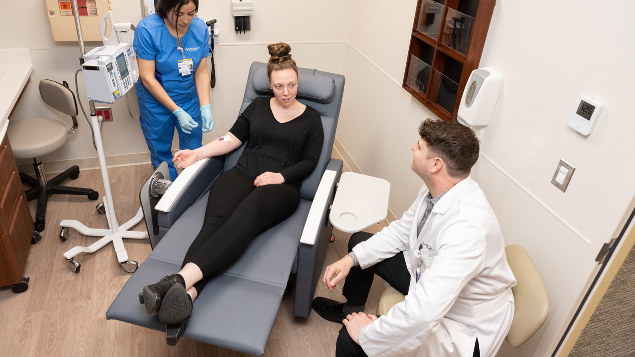 An aerial view of a physician and nurse speaking with a patient in a medical examination room. 