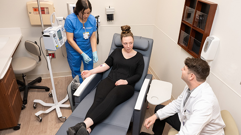 An aerial view of a physician and nurse speaking with a patient in a medical examination room. 