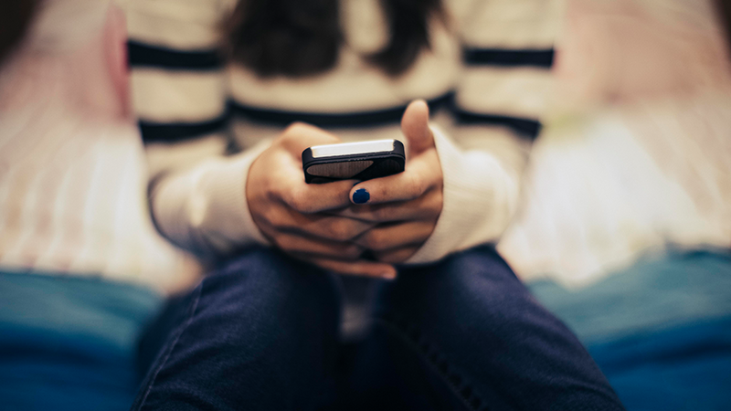Close up of teenage girl in a bedroom using a smartphone.