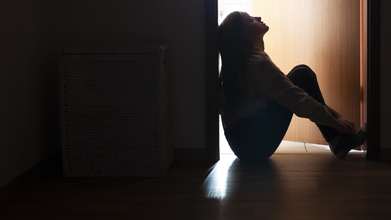 Distraught teenager sitting in the dark before a partly open door.