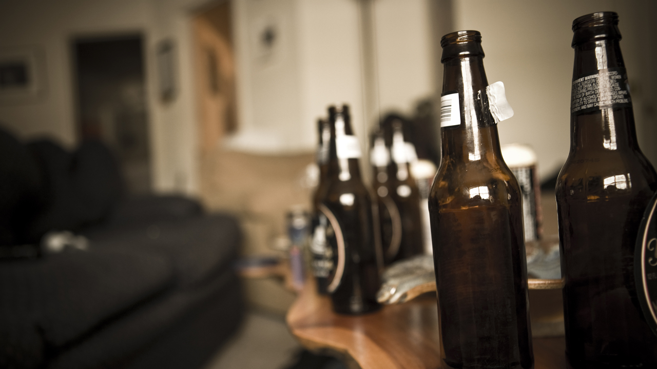 Bottles of open brown beer bottles on a wooden coffee table next to a brown sofa. 