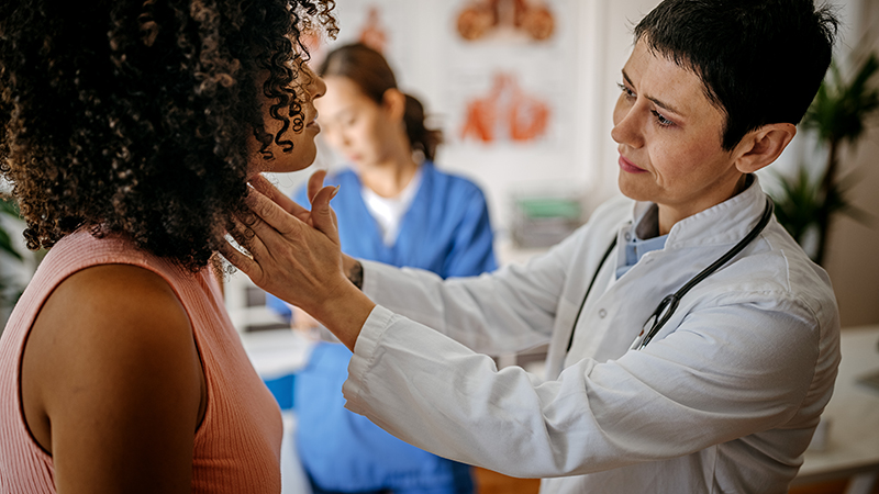 A physician examining a patient's thyroid with fingers on both sides of the patient's neck,