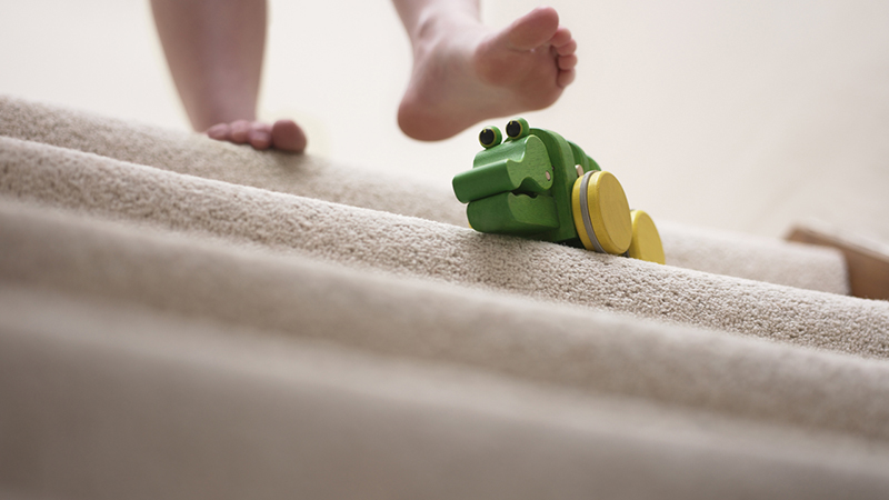 A bare foot stepping down a staircase, about to step onto a toy.