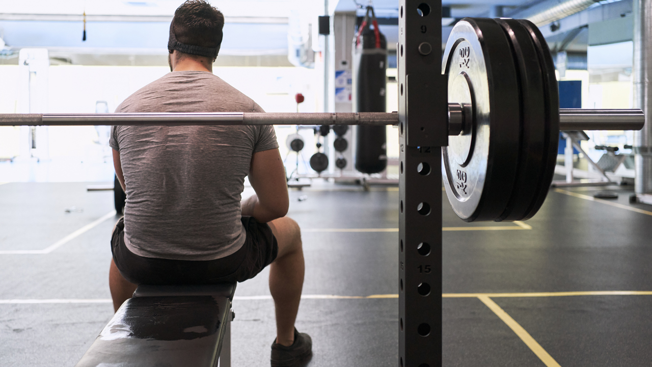 Person sitting on a gym bench with a barbell behind them.