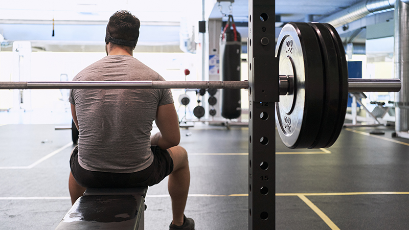 Person sitting on a gym bench with a barbell behind them.