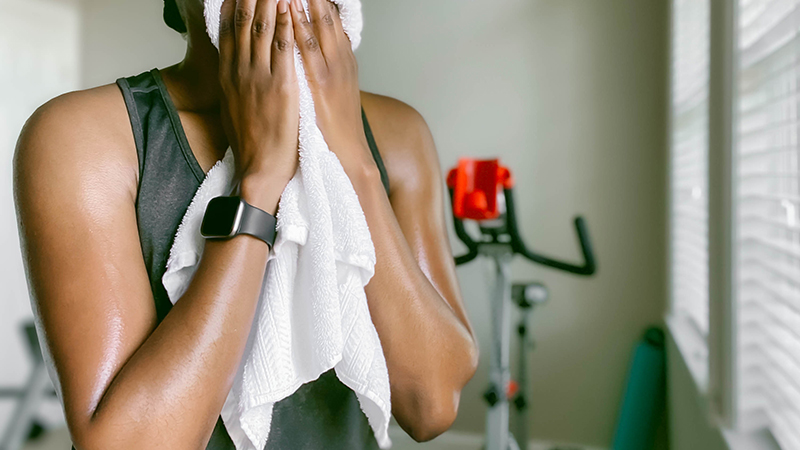 A sweaty person toweling off after a workout while wearing a smartwatch.
