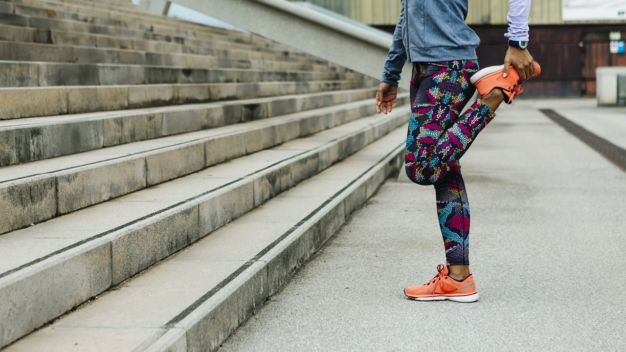 Person stands on one foot near steps doing a quad stretch outdoors