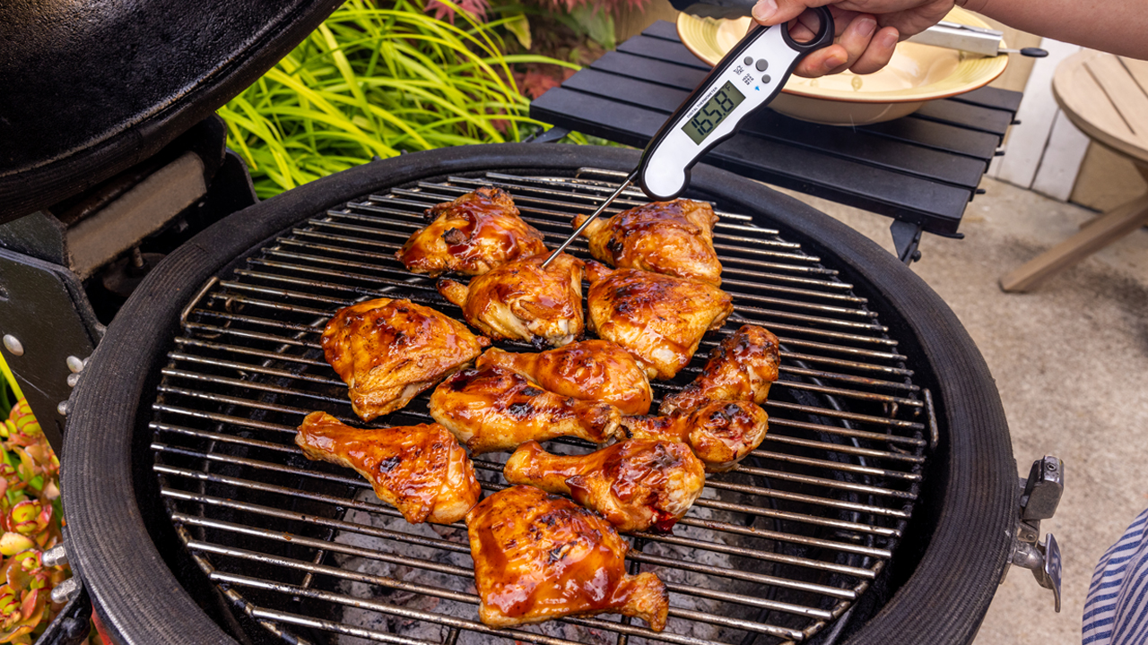 A meat thermometer with a reading of 165 degrees Fahrenheit in barbecue chicken on a grill.