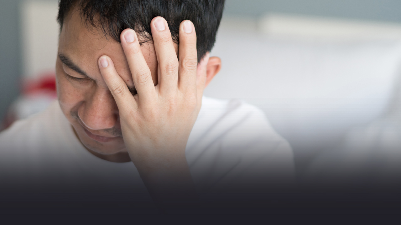 A man looking down in pain with his hand on his head. 