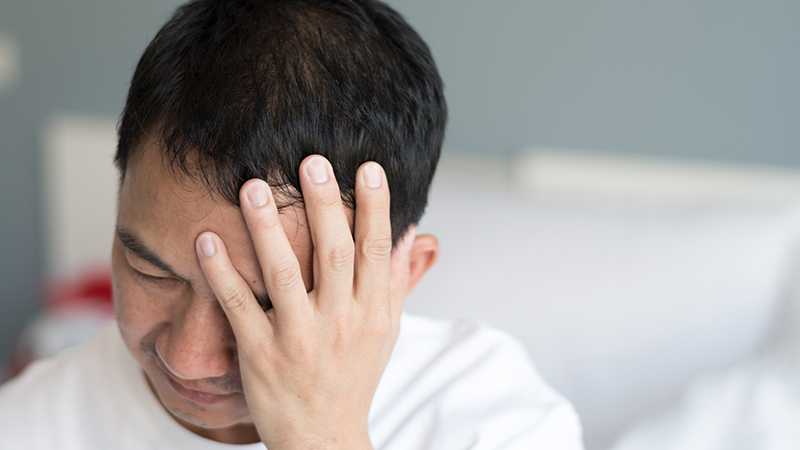 A man looking down in pain with his hand on his head. 