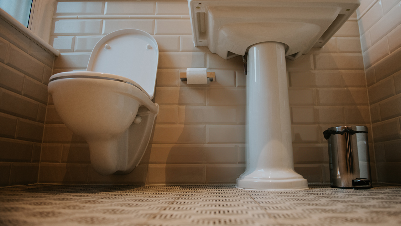 Picture taken at floor level of a sink and toilet in a white tiled bathroom. 