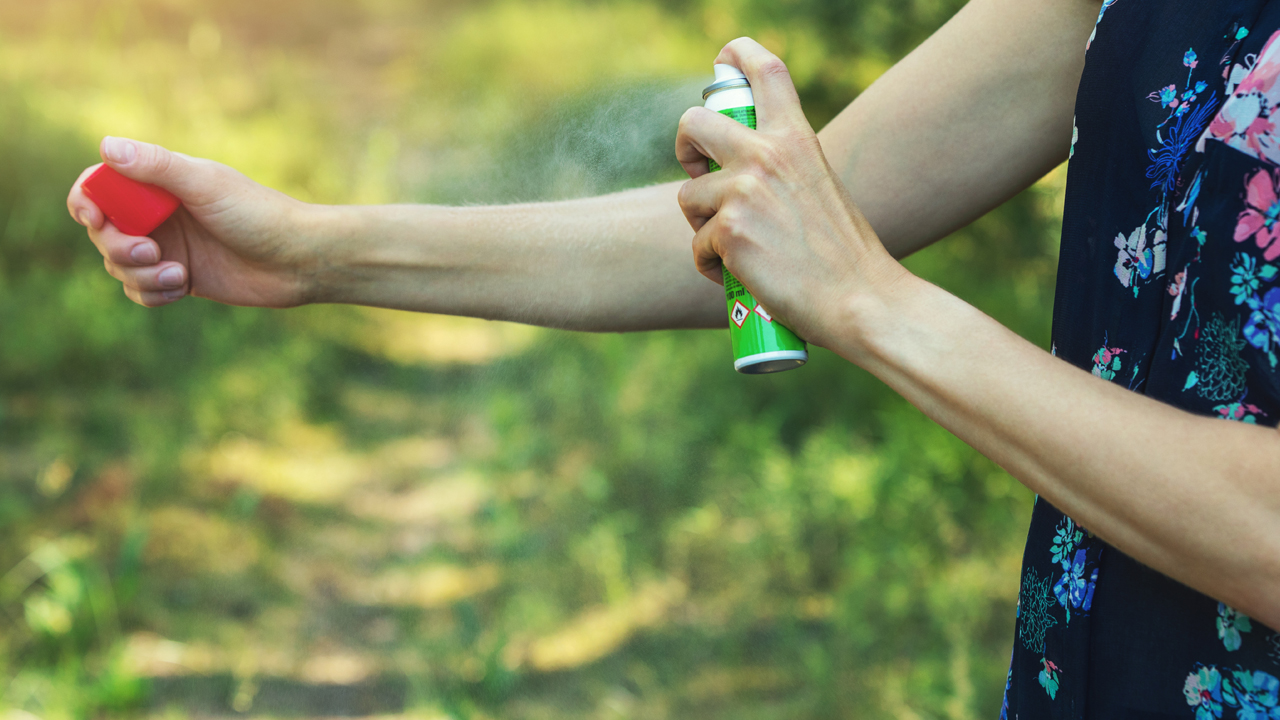 A person extends an arm to apply insect repellent outdoors. 