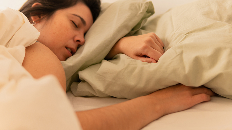 Person sleeping on their stomach with their face on a pillow and an arm beneath the pillow.