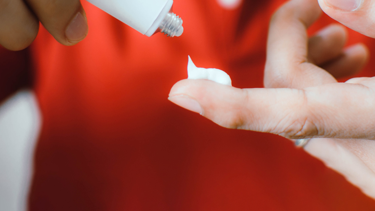 A closeup of a person putting medical ointment from a tube on their index finger.