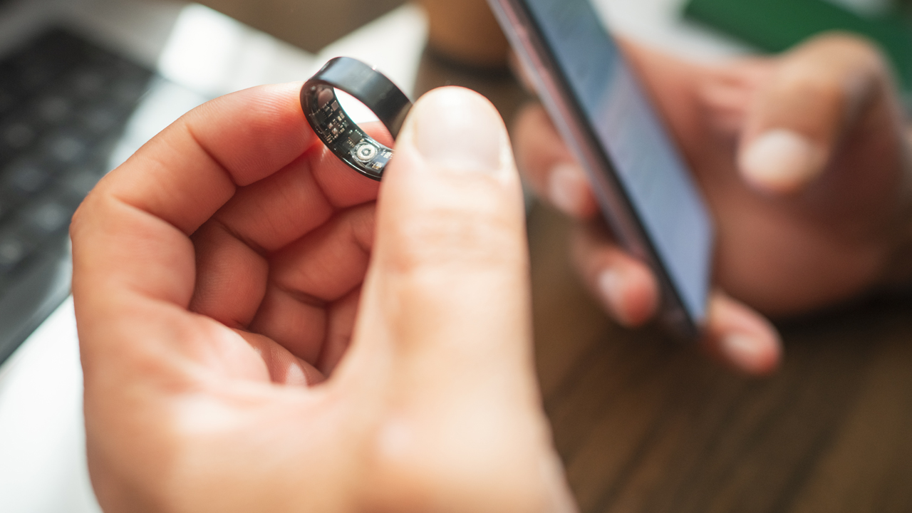 A person holding a smart ring and phone to track sleep.