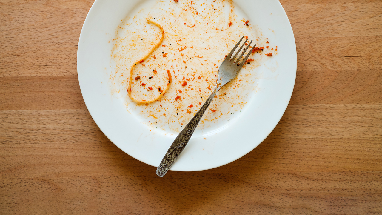 A dirty plate with one piece of pasta left behind.