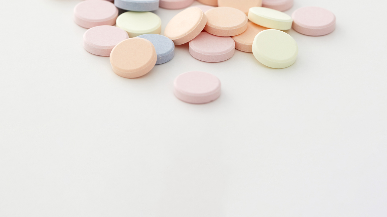 An assortment of colored antacid tablets on a light grey table. 